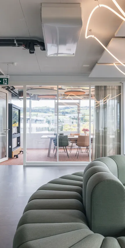 Großer Büro-Loungebereich mit geschwungenem Sofadesign und Panoramafenstern mit Blick auf die Umgebung.