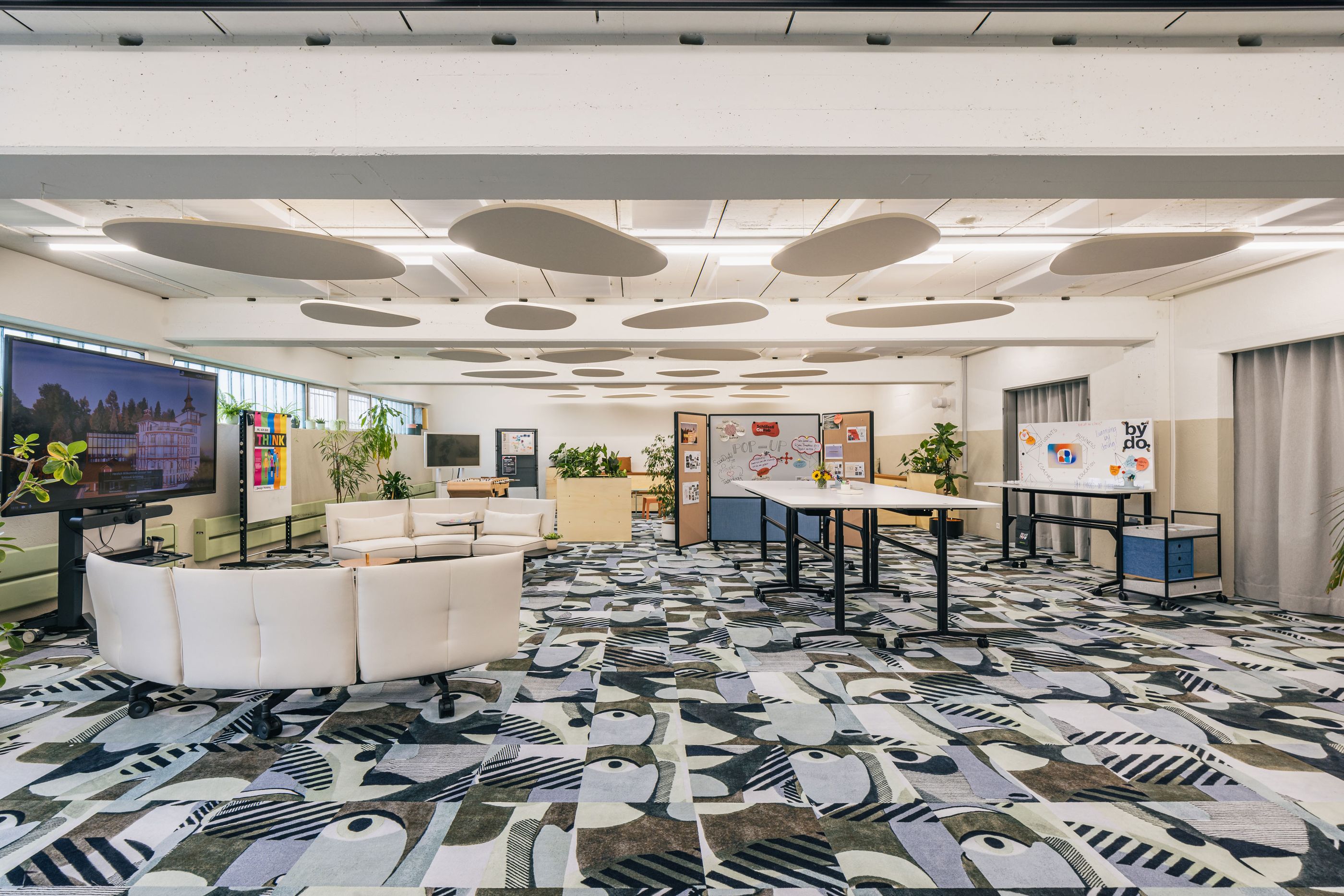 Heller Office-Community-Bereich mit Designsofa, Pflanzen und buntem Teppich.