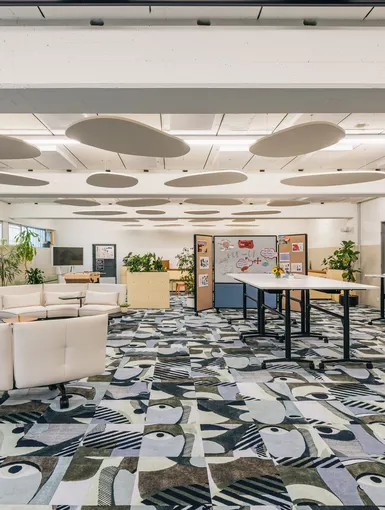 Heller Office-Community-Bereich mit Designsofa, Pflanzen und buntem Teppich.