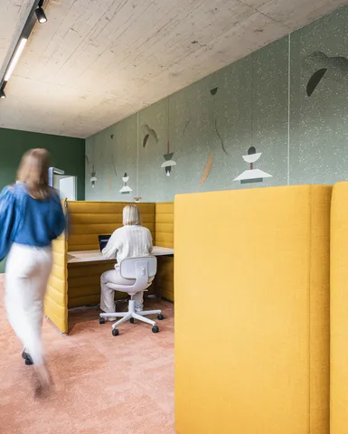 Ruhige Fokuszone mit gelben Akustik-Workpods, grün gestalteter Wand und warmem Teppichboden.