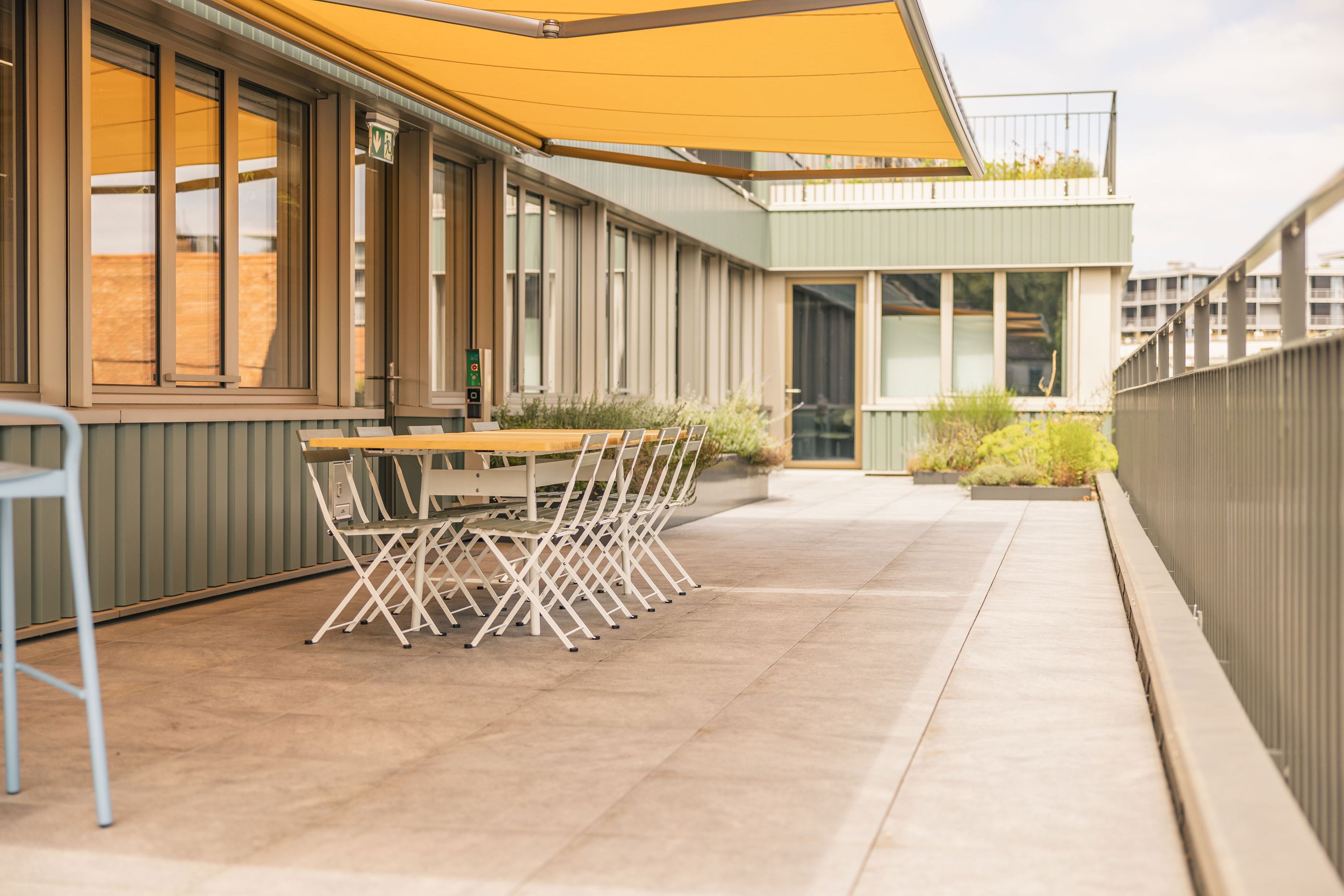 Großzügige Büro-Dachterrasse mit weißen Outdoor-Sitzmöbeln und Sonnenschutzmarkisen.