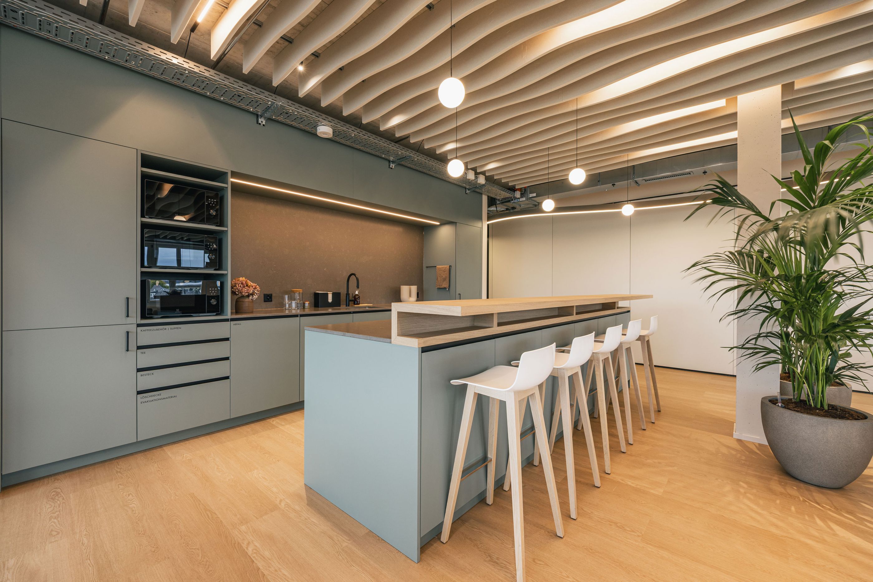 Moderne Küchenzeile mit hoher Arbeitsinsel, weißen Barhockern und hängenden Kugelleuchten.