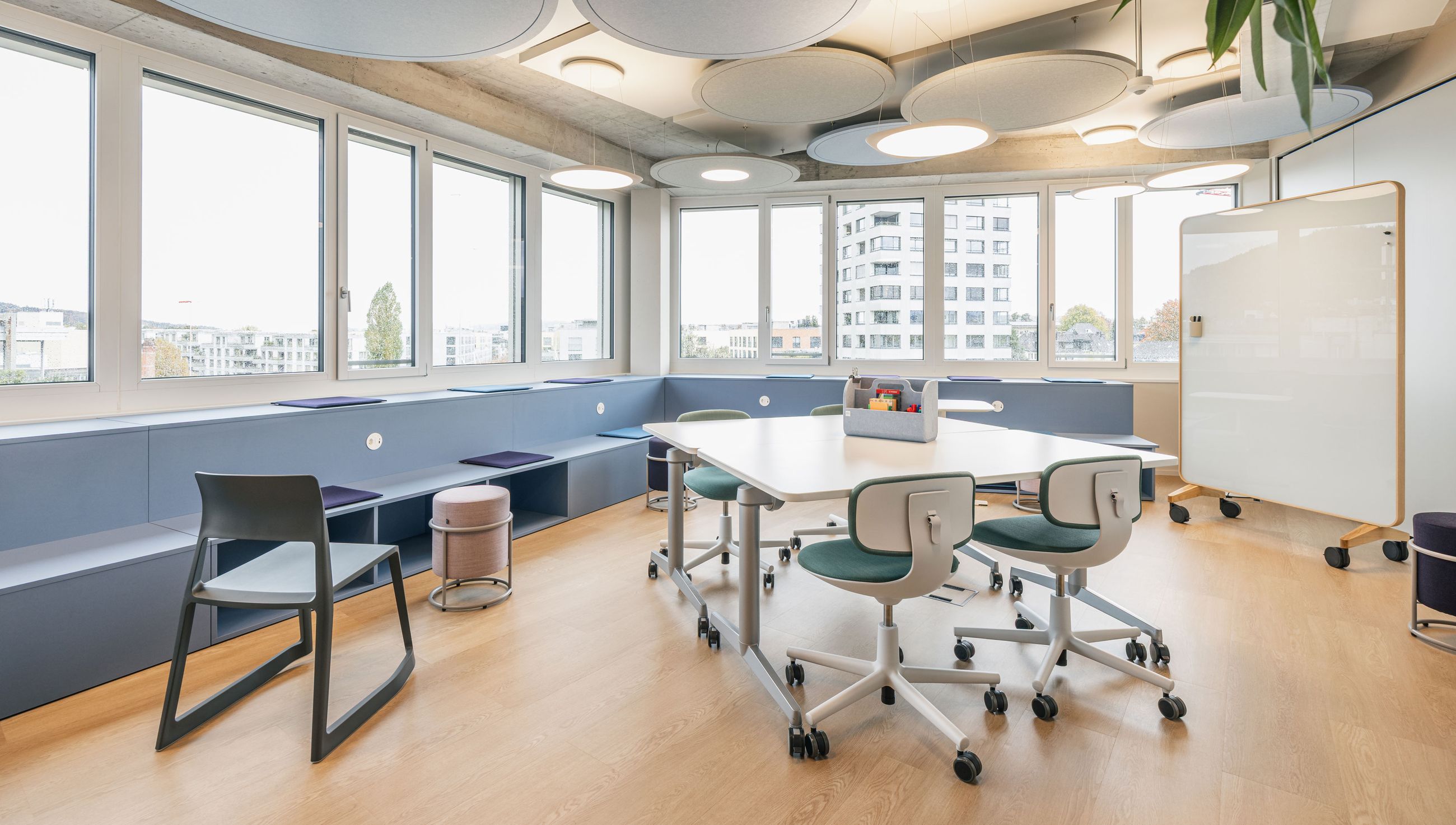 Lichtdurchfluteter Kreativraum mit runden Akustikelementen an der Decke, flexiblen Tischen und Whiteboard.