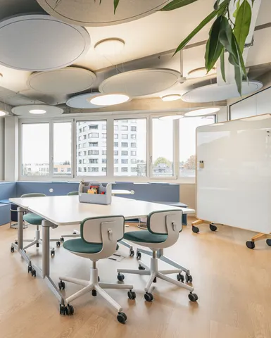 Lichtdurchfluteter Kreativraum mit runden Akustikelementen an der Decke, flexiblen Tischen und Whiteboard.