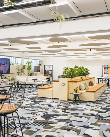 Offener Meetingbereich mit Pflanzen, Holzpodesten und großem Bildschirm.