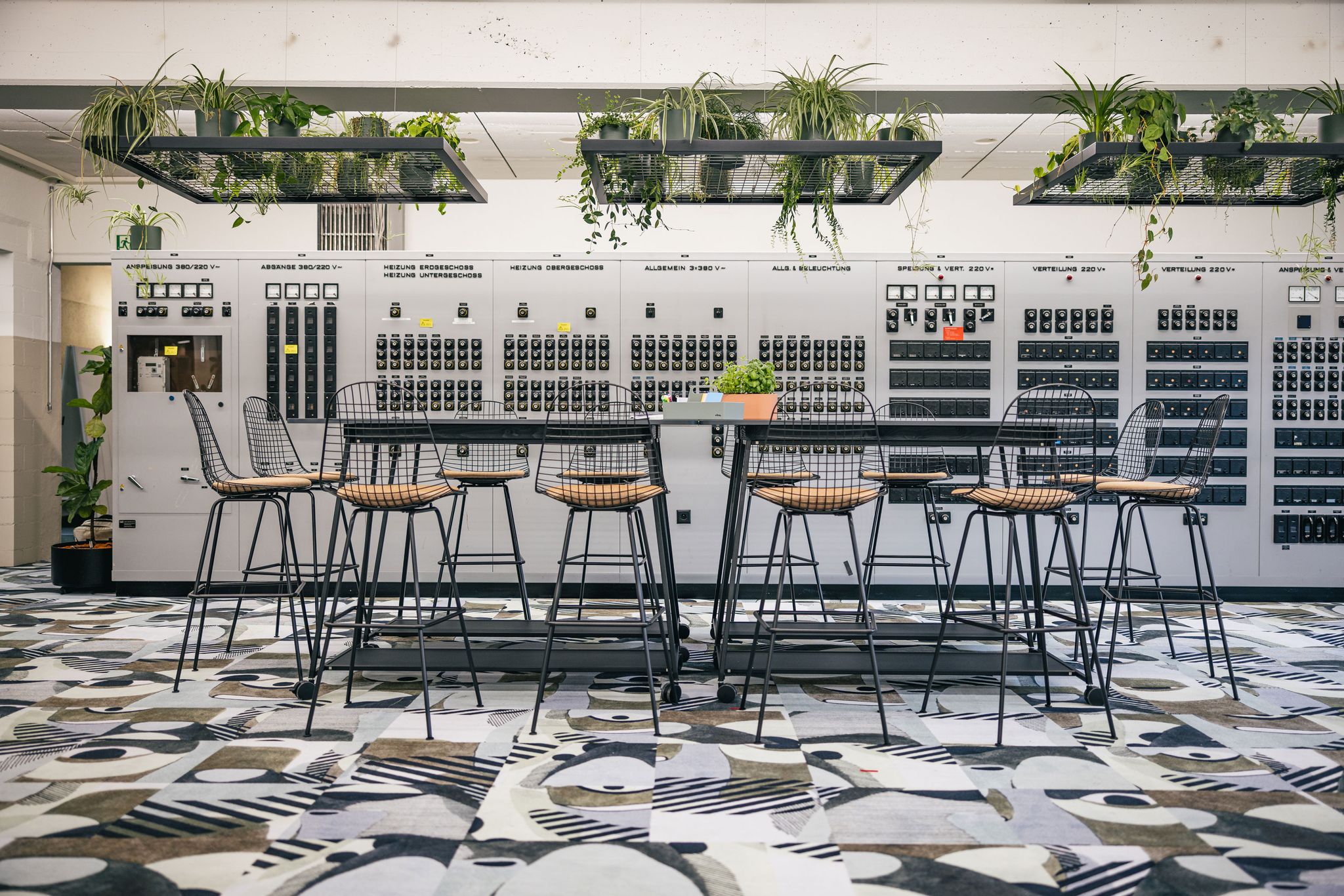 Workshopzone mit großem Tisch, schwarzen Stühlen und farbigem Teppich.