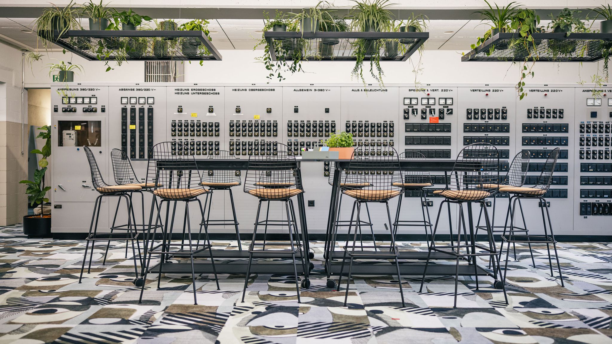 Workshopzone mit großem Tisch, schwarzen Stühlen und farbigem Teppich.