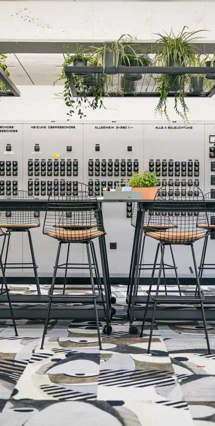 Workshopzone mit großem Tisch, schwarzen Stühlen und farbigem Teppich.