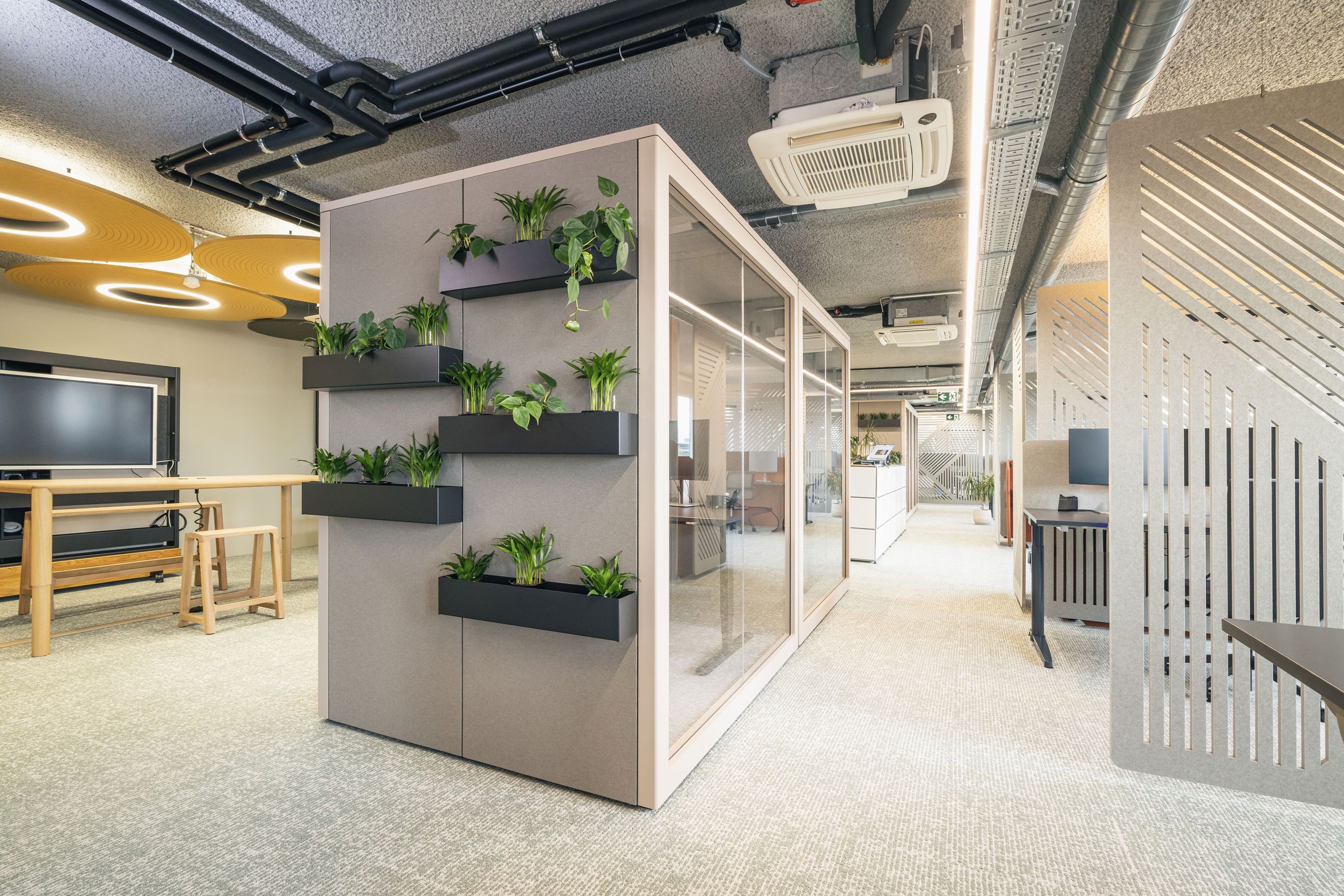 Innovativer Büroarbeitsbereich mit gläserner Meetingbox und vertikalem Pflanzensystem.