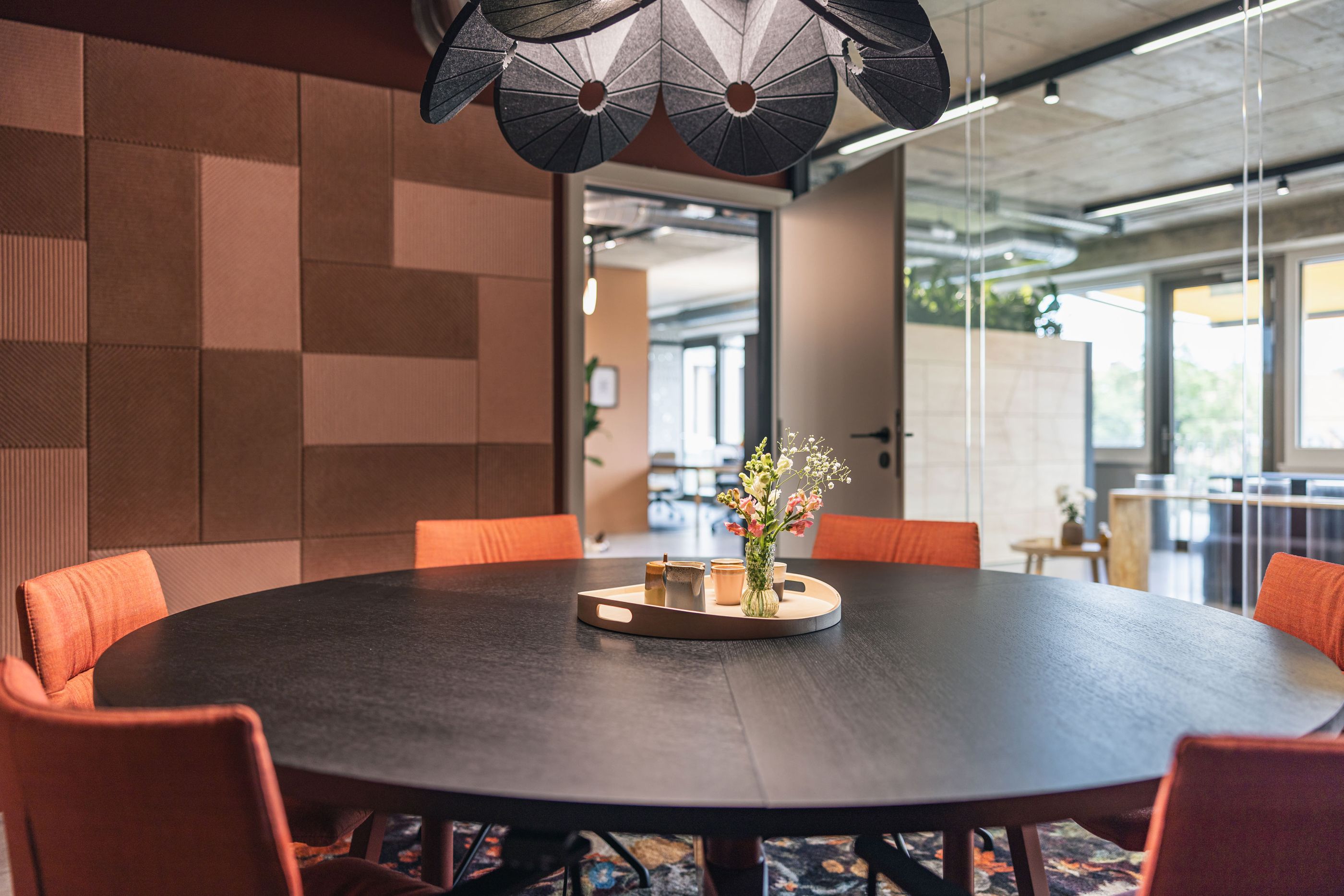 Eleganter Meetingraum mit rundem schwarzem Tisch, dekorativer Wandverkleidung und Blumenarrangement.