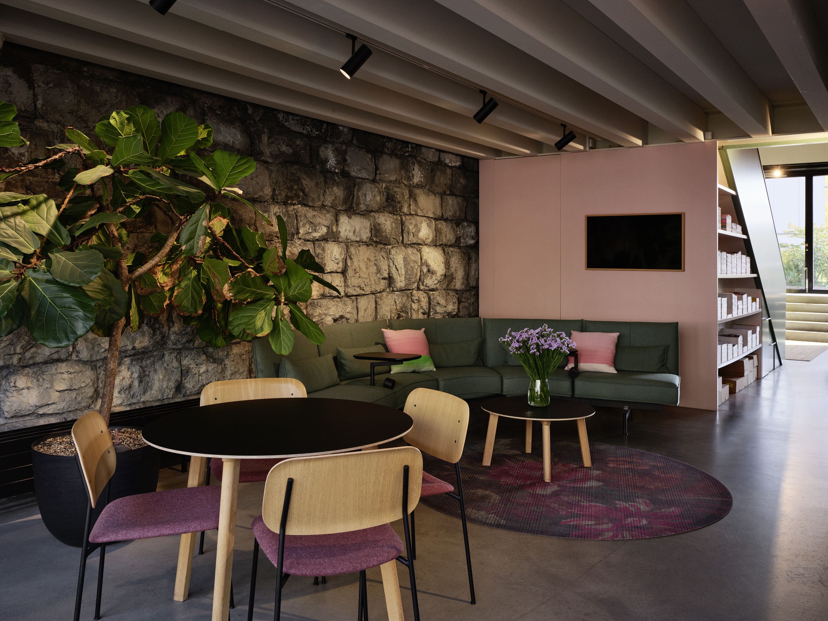 Gemütlicher Büro-Loungebereich mit grünem Sofa, Holzstühlen und kleinen Beistelltischen im Tageslicht.