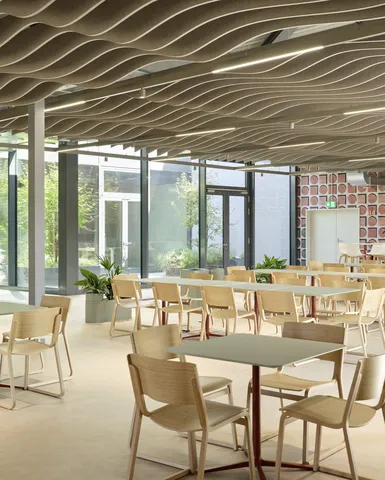 Cafeteria mit Bestuhlung und grünen Tischen.