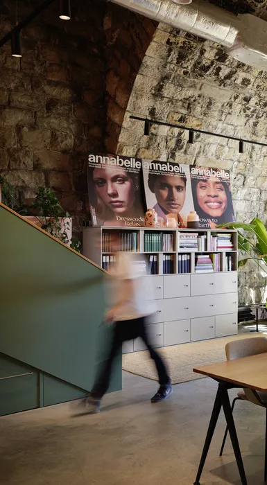 Moderner Besprechungsbereich mit hellem Holztisch und minimalistischem Hocker in warmem Office-Design.