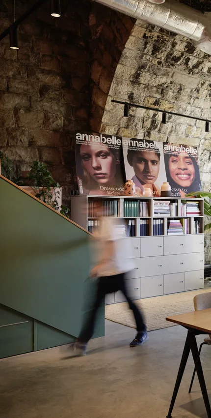 Moderner Besprechungsbereich mit hellem Holztisch und minimalistischem Hocker in warmem Office-Design.