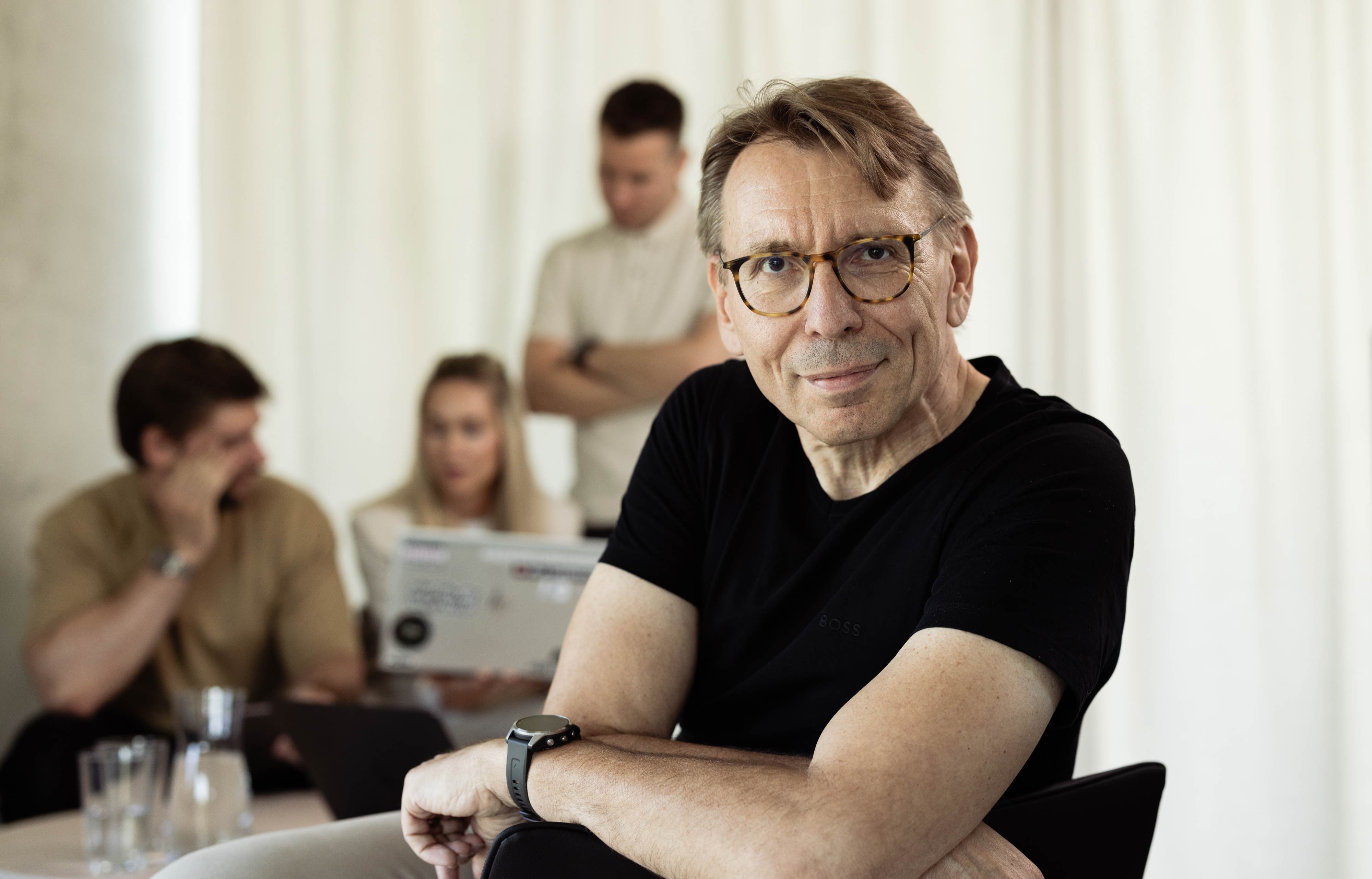 Handsome young man sitting in the front and behind him the three consultants are discussing a project.