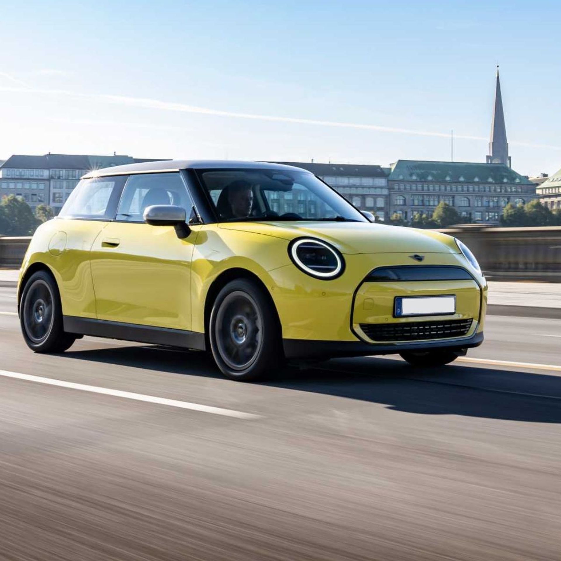 Ein gelbes Modell des Mini Cooper E fährt über eine Brücke.