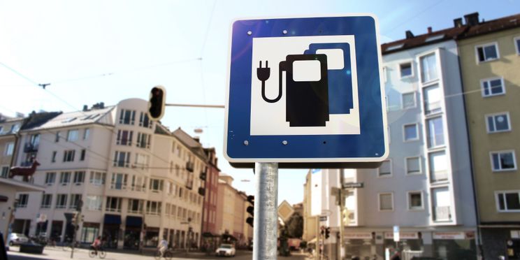 Ein Schild in einer Innenstadt bildet zwei Ladesäulen ab, die den Parkplatz als Ladeplatz für E-Autos kennzeichnen.