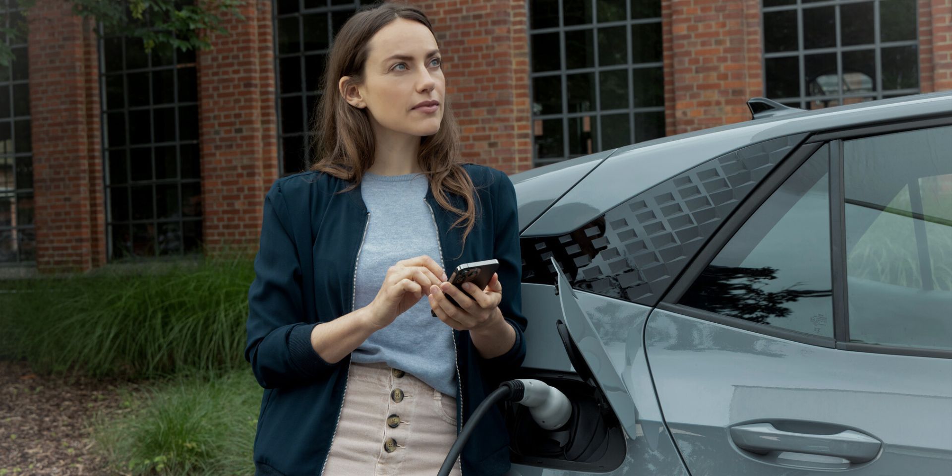 Frau hält Smartphone in der Hand, während e-Auto lädt.