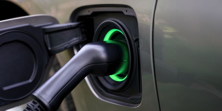 Nahaufnahme eines angeschlossenen Ladekabels an ein e-Auto mit grünem Leuchtsymbol.ing plug inserted into the port, surrounded by a glowing green light.