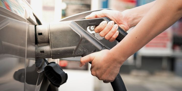 Nahaufnahme von Händen, die einen Elektroauto Ladestecker halten.