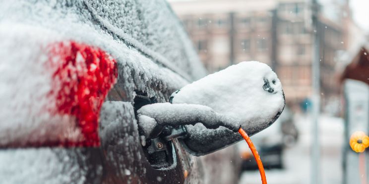 Geparktes Elektroauto ist mit Schnee bedeckt und mit der Ladesäule per Kabel verbunden.
