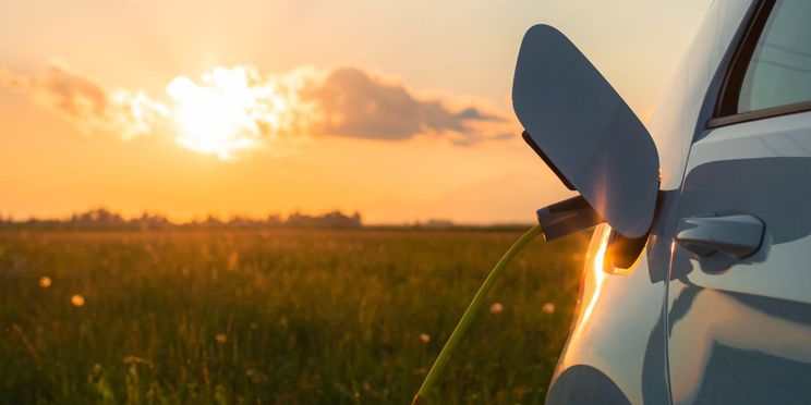 Elektrisches Auto ist an Ladekabel angeschlossen. Im Hintergrund geht die Sonne unter.