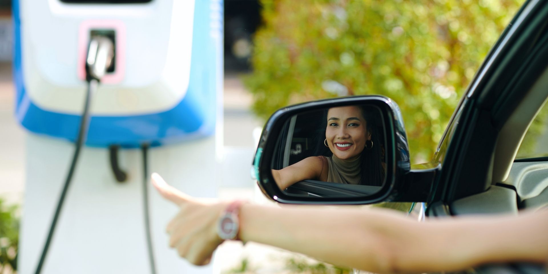 Frau sitzt im Elektroauto und streckt den Arm mit Daumen nach oben aus dem Fahrerfenster.