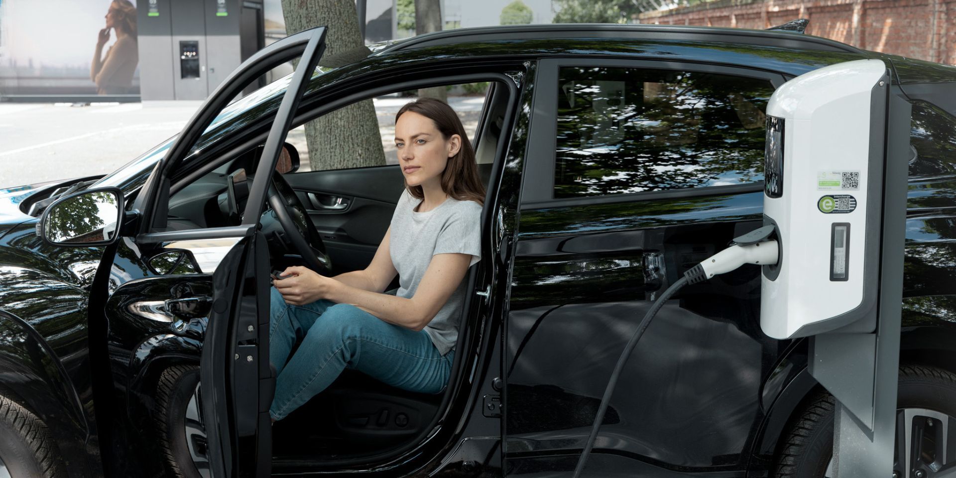 Frau sitzt im schwarzen e-Auto, während dieses an einer öffentlichen Ladestation lädt.