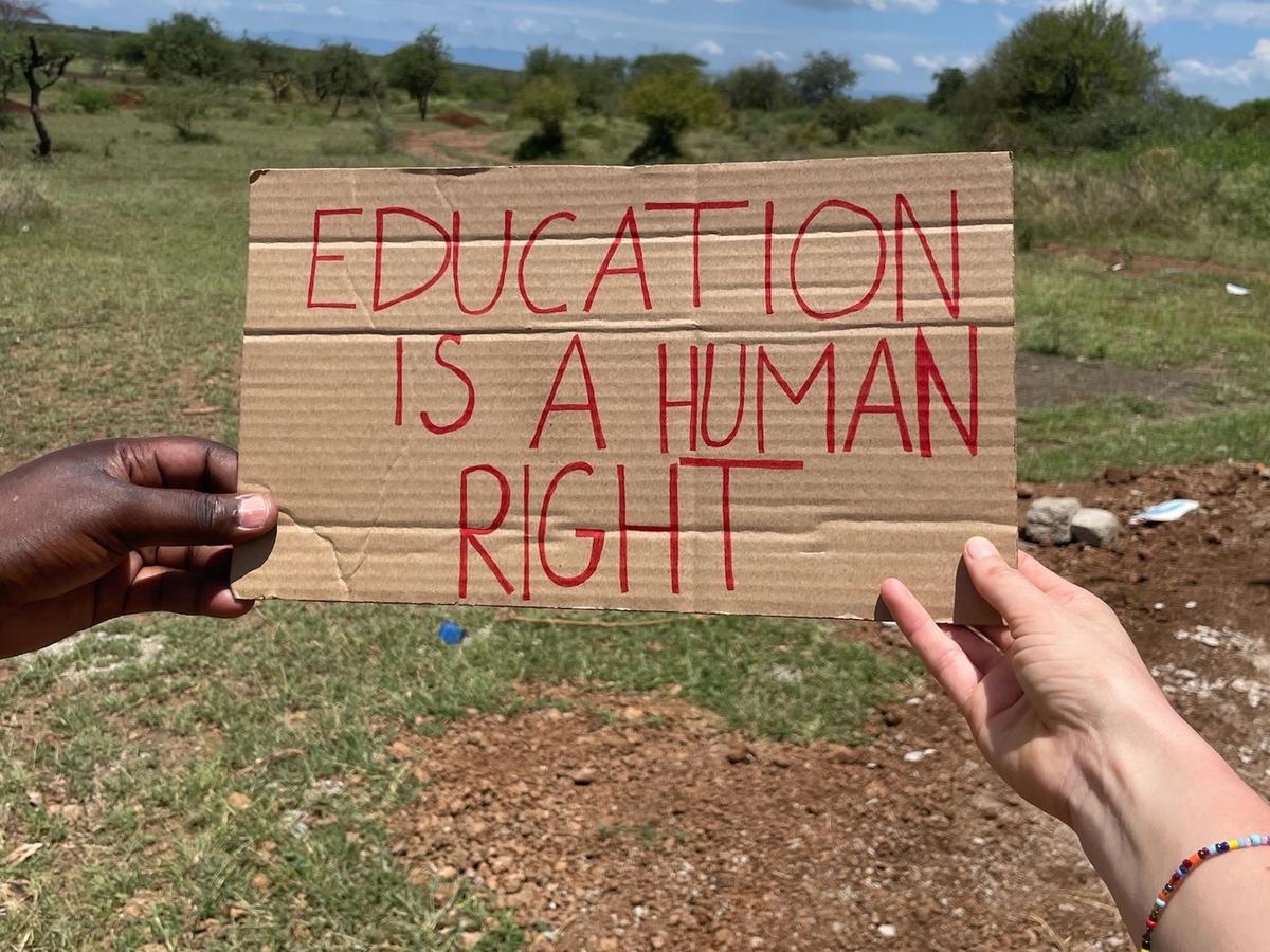 Zwei Hände halten ein Pappschild mit der Aufschrift „Education is a human right“ in die Landschaft.