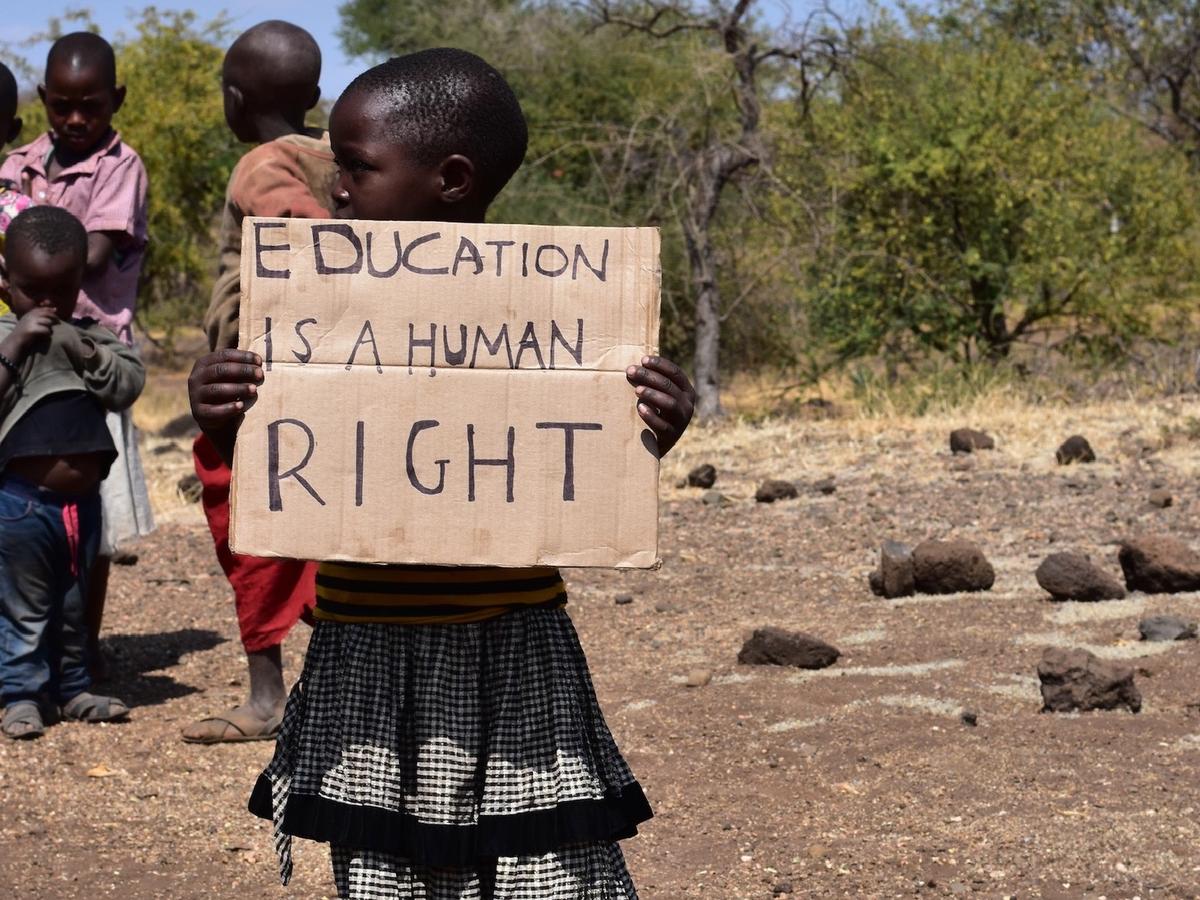 Ein Mädchen trägt das Pappschild mit der Aufschrift „Education is a human right“ über den Weg.
