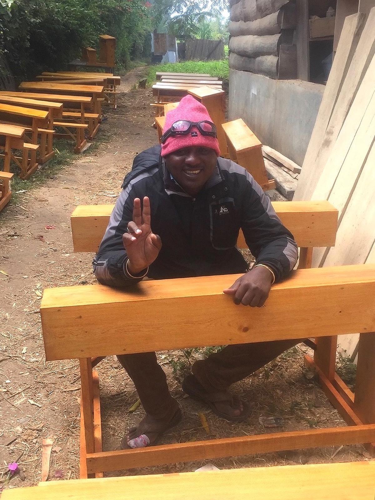 Lalahe sitzt lachend hinter frisch gezimmerten Schulbänken aus hellem Holz.