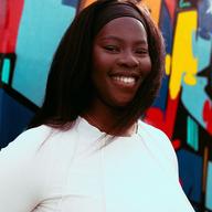 Smiling woman wearing a white top and headband in front of a colorful graffiti wall.