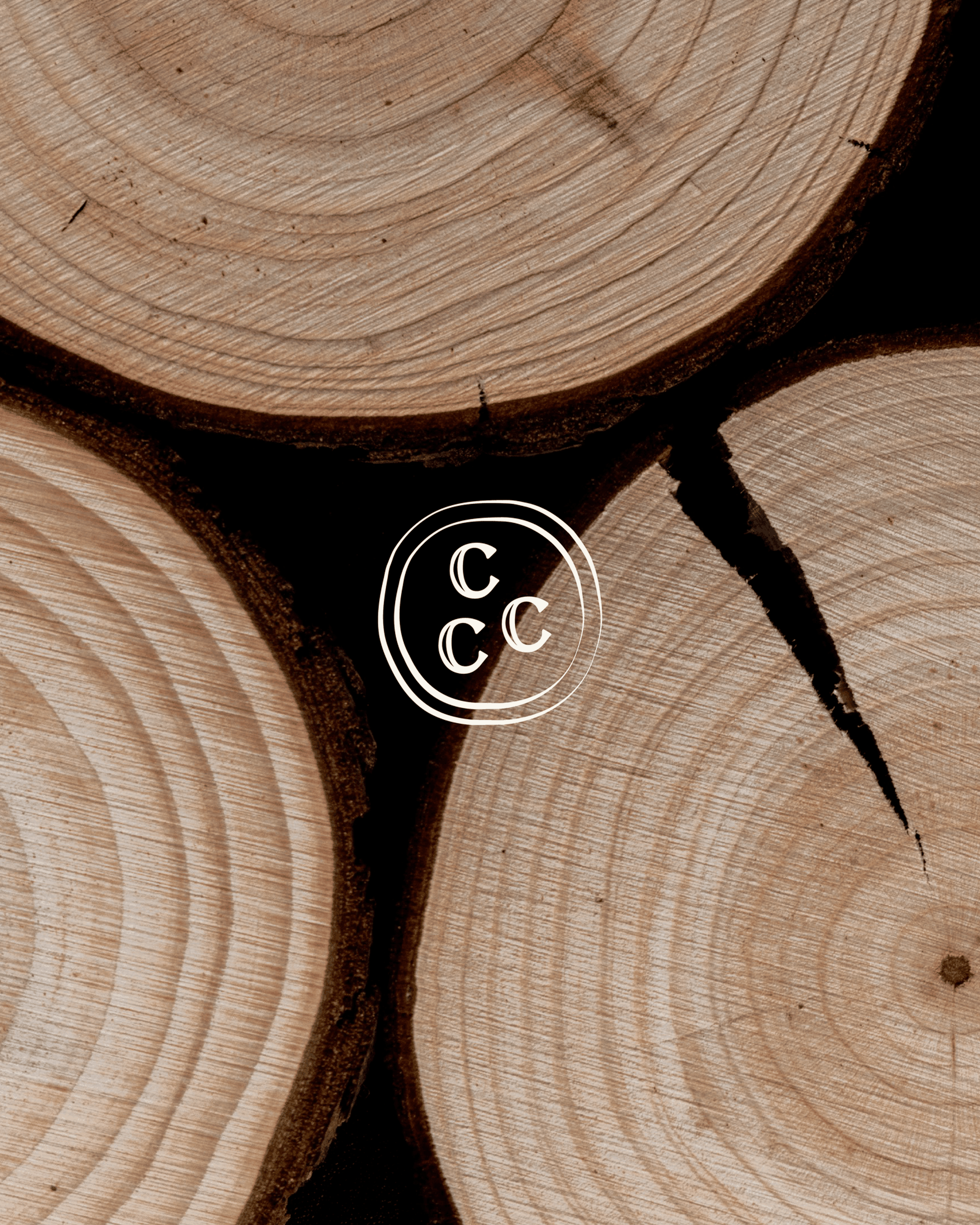 Close-up of cut tree log cross-sections with visible rings and cracks, featuring a light logo with three "C"s in the center.
