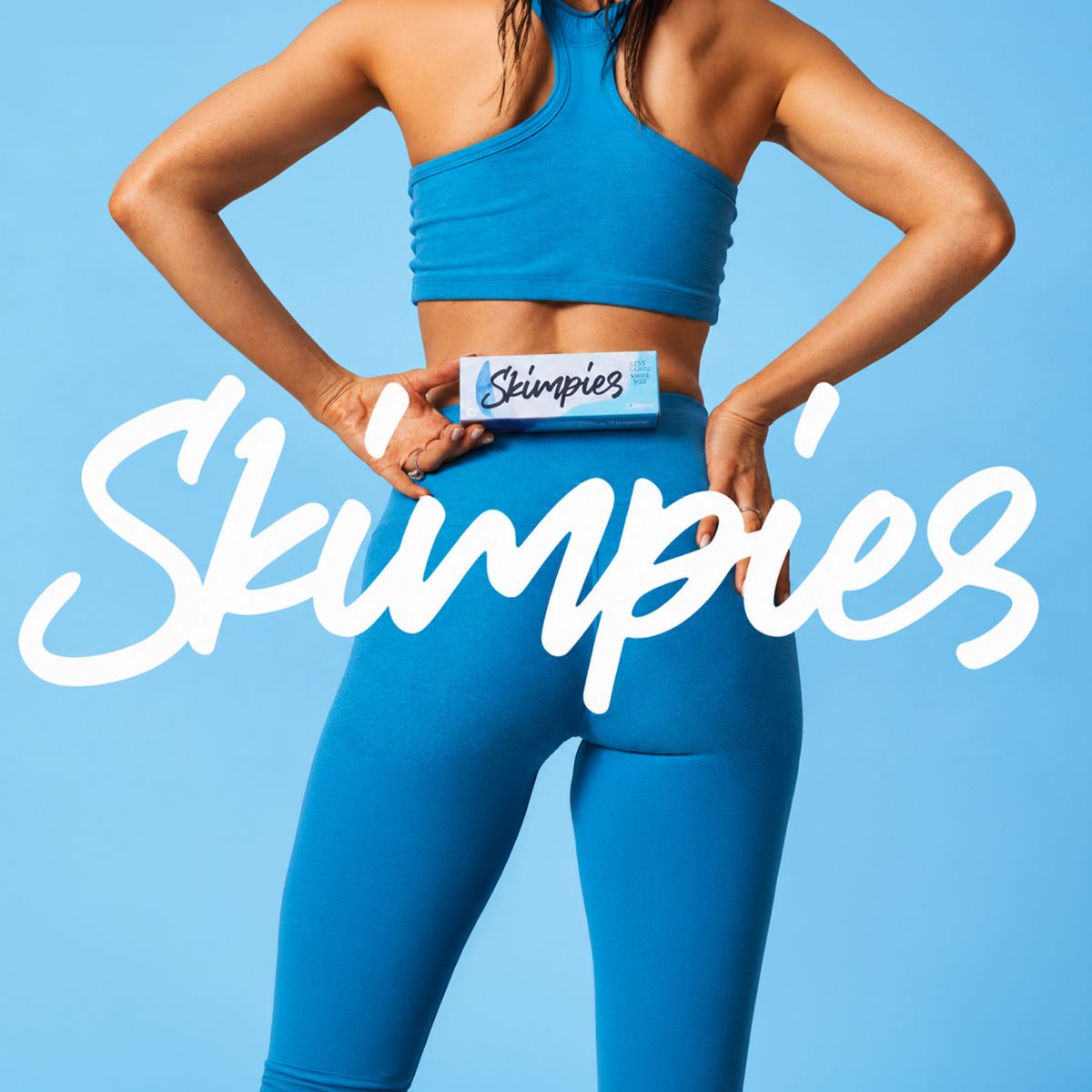 Model in blue activewear seen from behind, holding a Skimpies liner box at her waist under the white Skimpies script logo