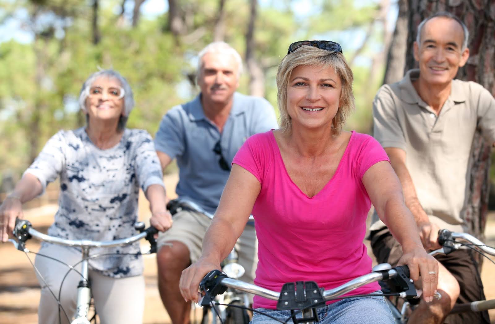 Group of happy senior adults having fun and cycling together in a retirement home. Several cheerful old men and women smiling on their bicycles taking a ride on a sunny, beautiful day