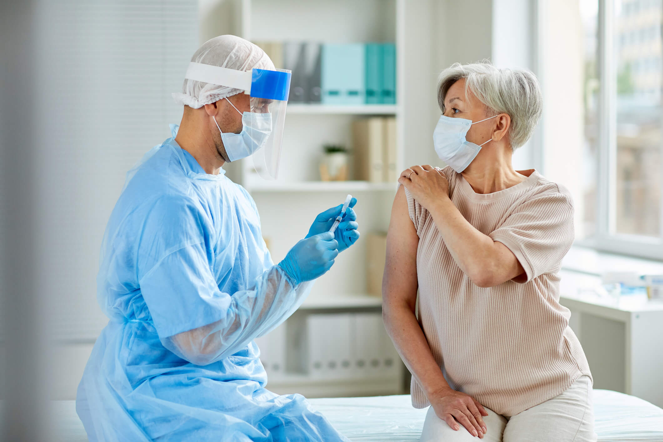 Patient getting shot from doctor while both wear masks