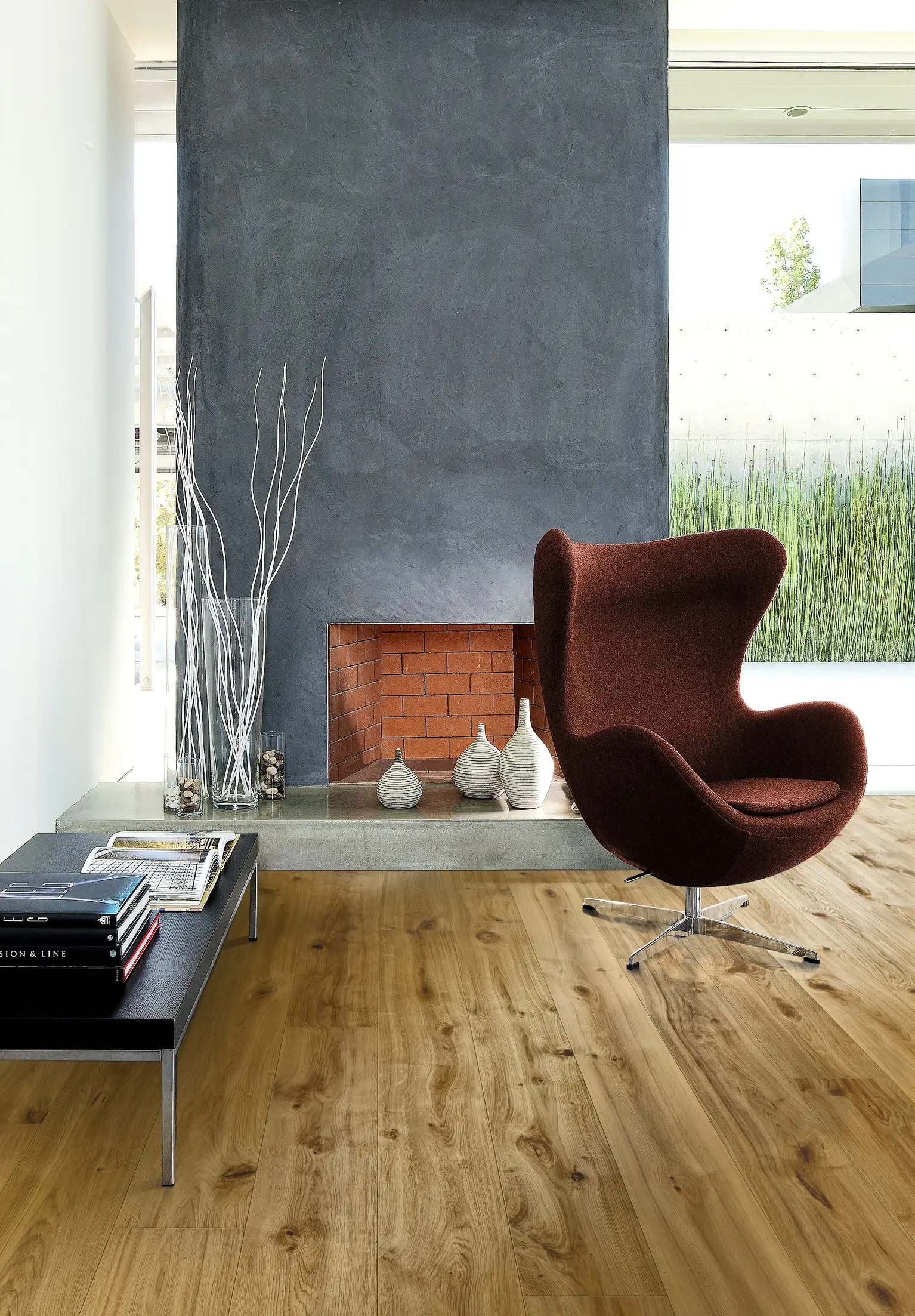 Modern living room with a dark gray fireplace, brown egg chair, wooden floor, and a minimalist bench with books and vases.