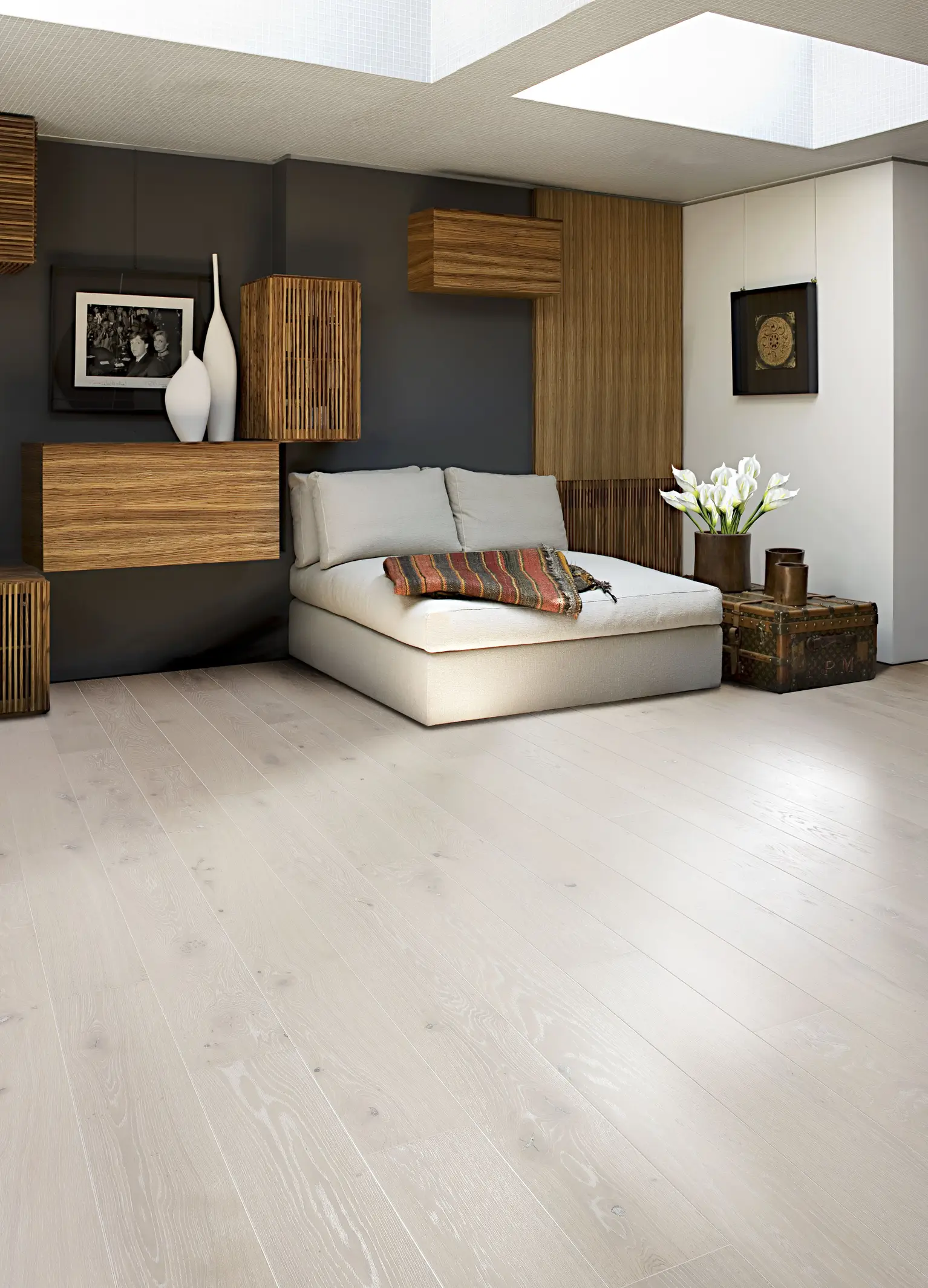 Modern living room with light wood flooring, a beige sofa, decorative wooden wall accents, and vases on shelves. A skylight illuminates the space.