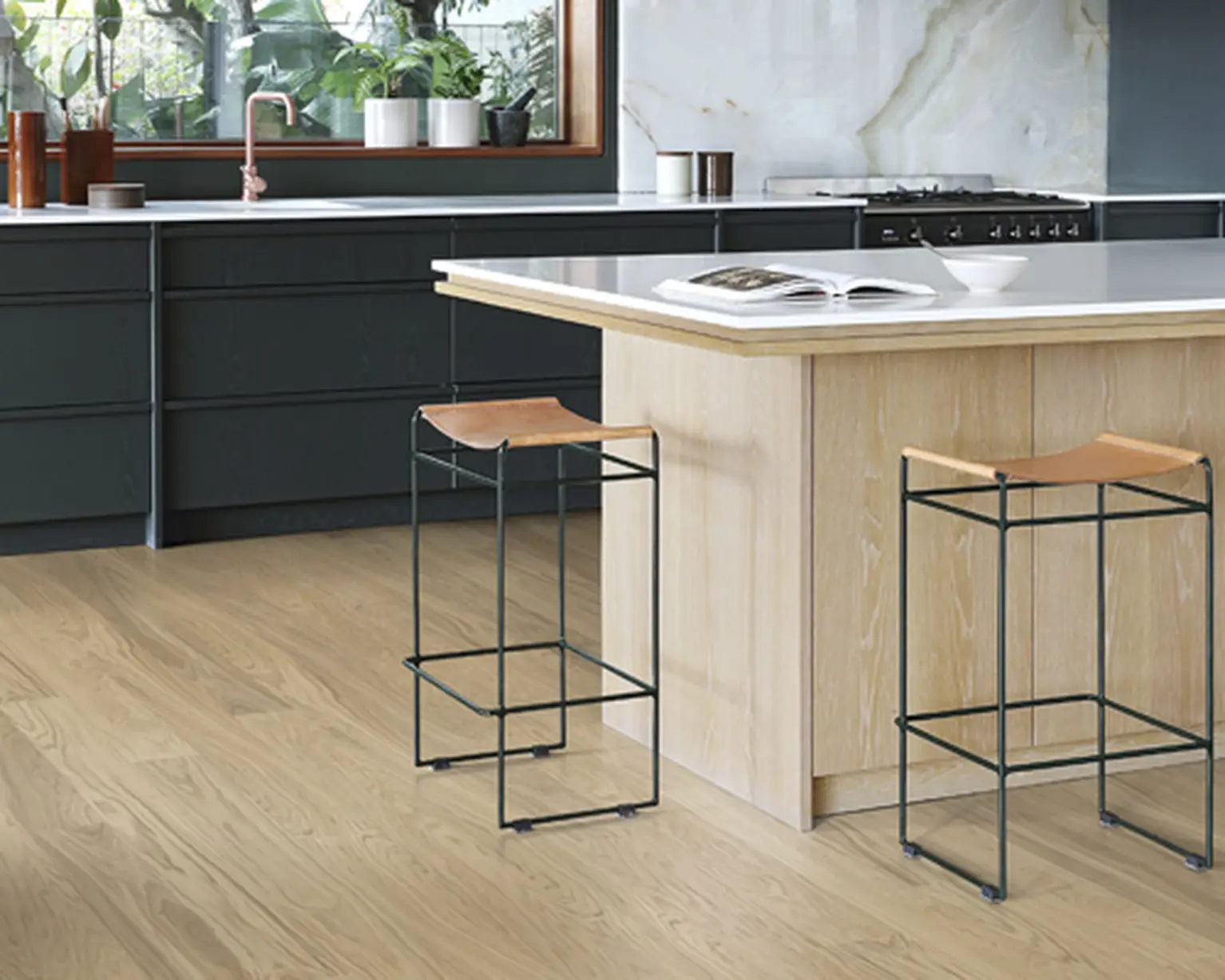 Kitchen with light wood flooring, dark cabinetry, and a large island with stools.