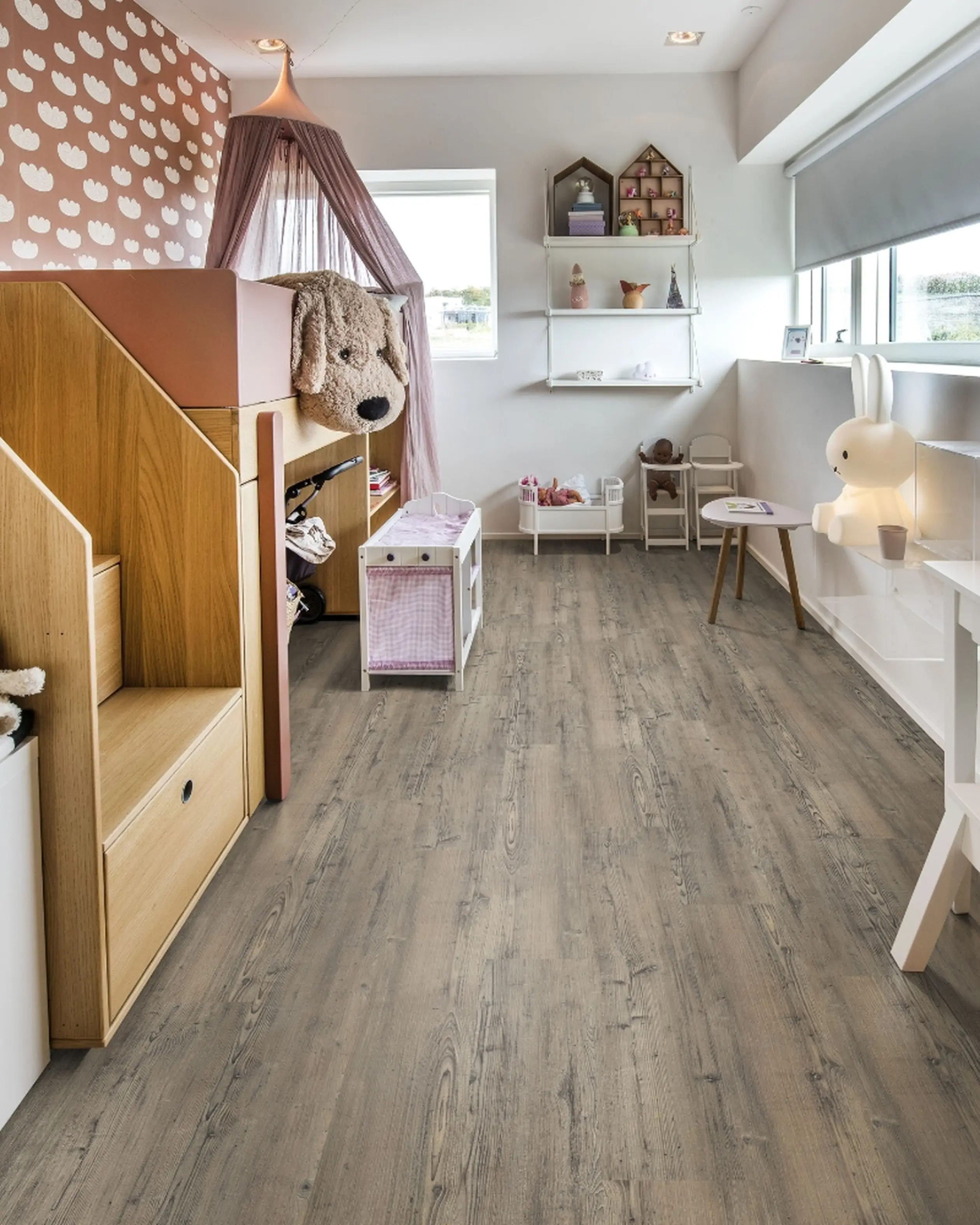 A cozy children's bedroom with gray-brown wooden flooring, pastel decor, and a built-in bed featuring a large plush dog.