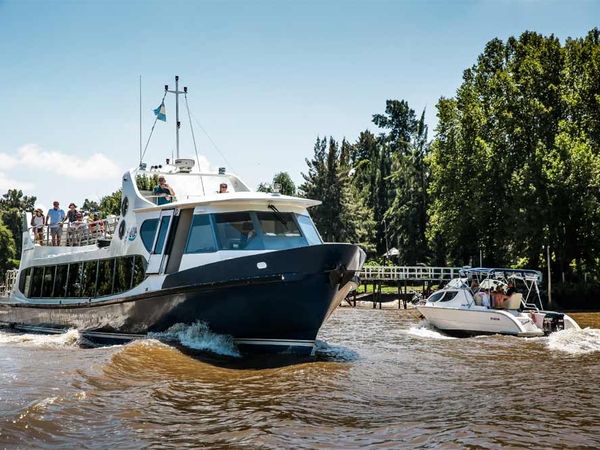 Modern passenger ferry boat navigating the scenic waterways of Tigre, Buenos Aires, with tourists aboard and smaller boats nearby.