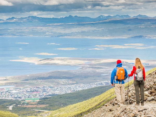 Two hikers with backpacks overlook Ushuaia and the Beagle Channel from Glaciar Martial in Tierra del Fuego.