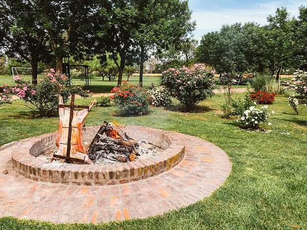 Brick firepit with roasting equipment in a lush garden surrounded by blooming roses at an estancia in San Antonio de Areco, Buenos Aires.