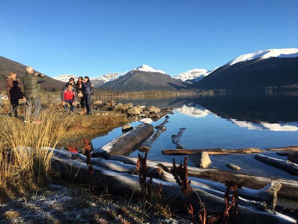 Visitors admire snow-capped mountains reflected in the pristine waters of Lago Fagnano in Tierra del Fuego, Patagonia.