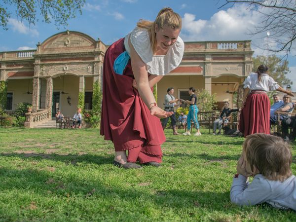 Woman in traditional Argentine dress entertains a child on the lawn of a historic estancia in San Antonio de Areco.