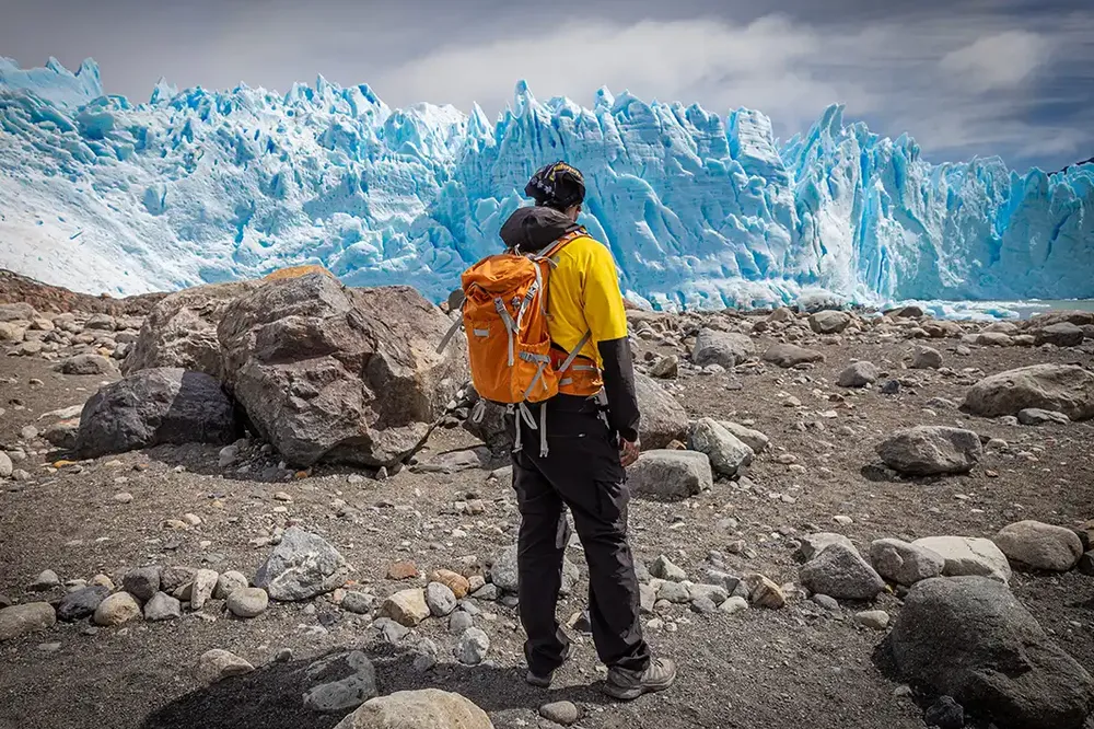 Hiker with orange backpack viewing the stunning turquoise ice formations of Perito Moreno Glacier in El Calafate, Patagonia.
