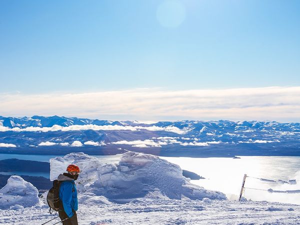 Skier overlooking snow-covered peaks and a frozen lake in the Andes mountains near Bariloche, Argentina.