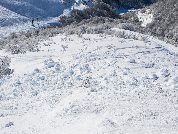 Skier's view down snowy slope at Catedral ski resort near Bariloche with forested valleys and mountains below.