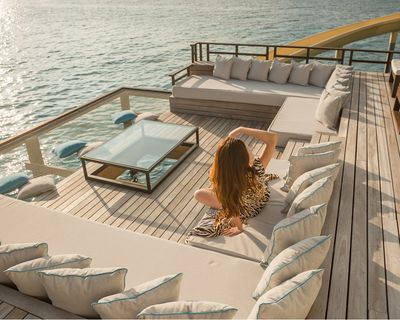 Woman relaxing on a sunlit deck of a luxury yacht with turquoise ocean waters and comfortable seating areas.