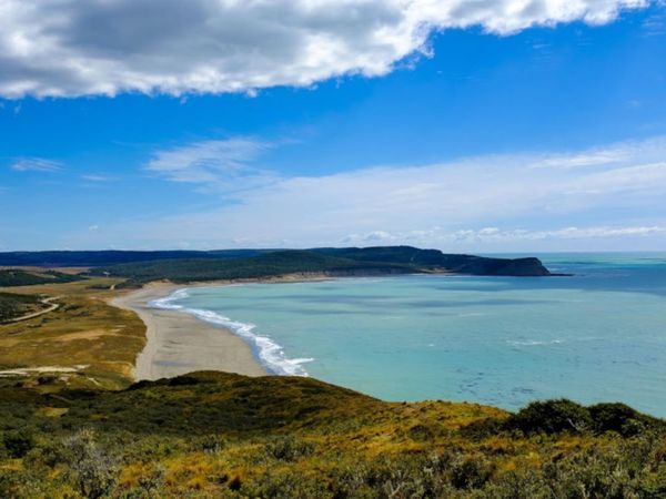 Turquoise waters and sandy beach curve along Cabo San Pablo's rugged coastline under a bright blue sky.